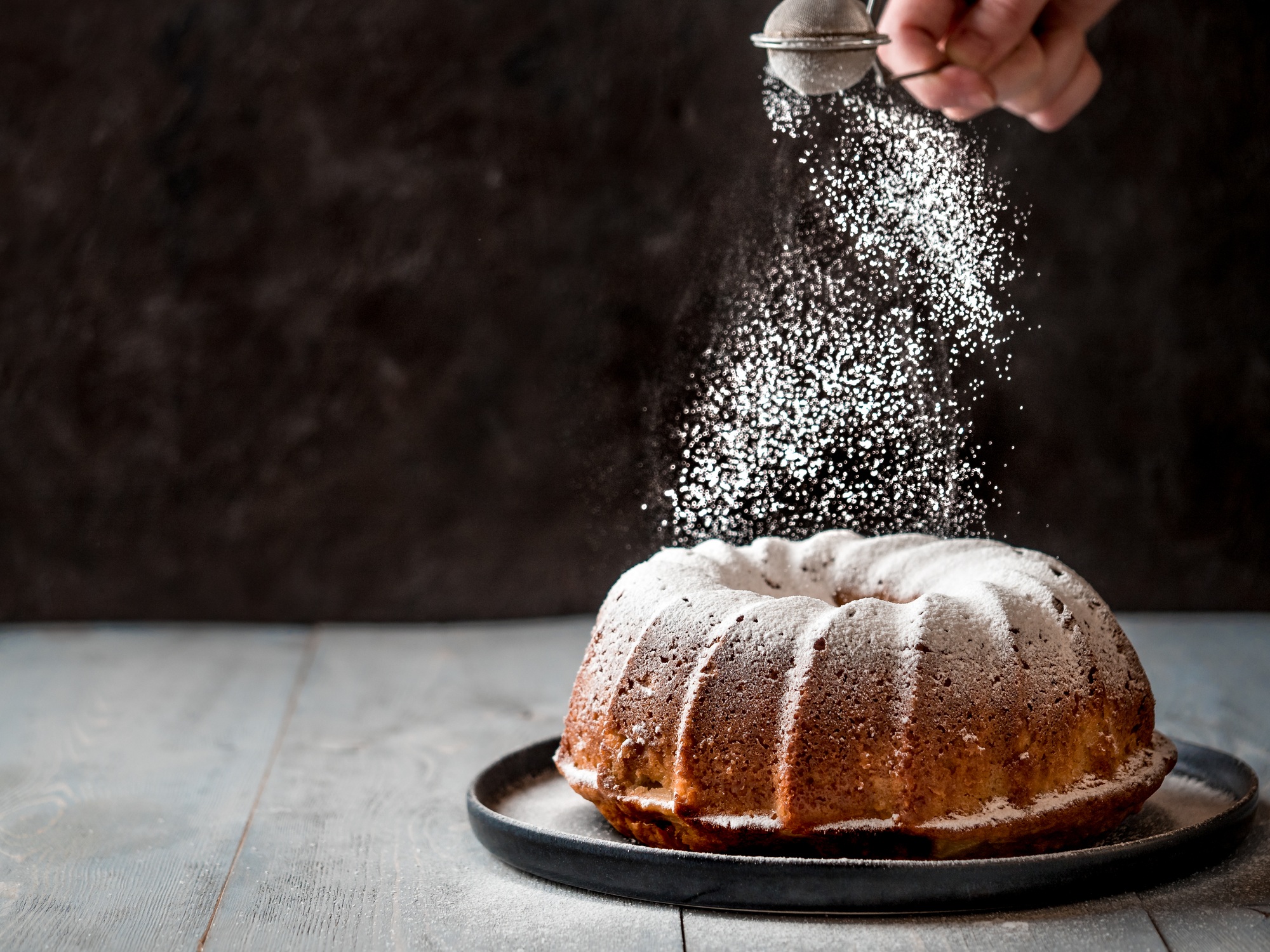 Female hand sprinkling icing sugar on muffin cake