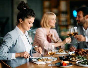 Happy businesswoman eating while having lunch with coworkers in a restaurant.