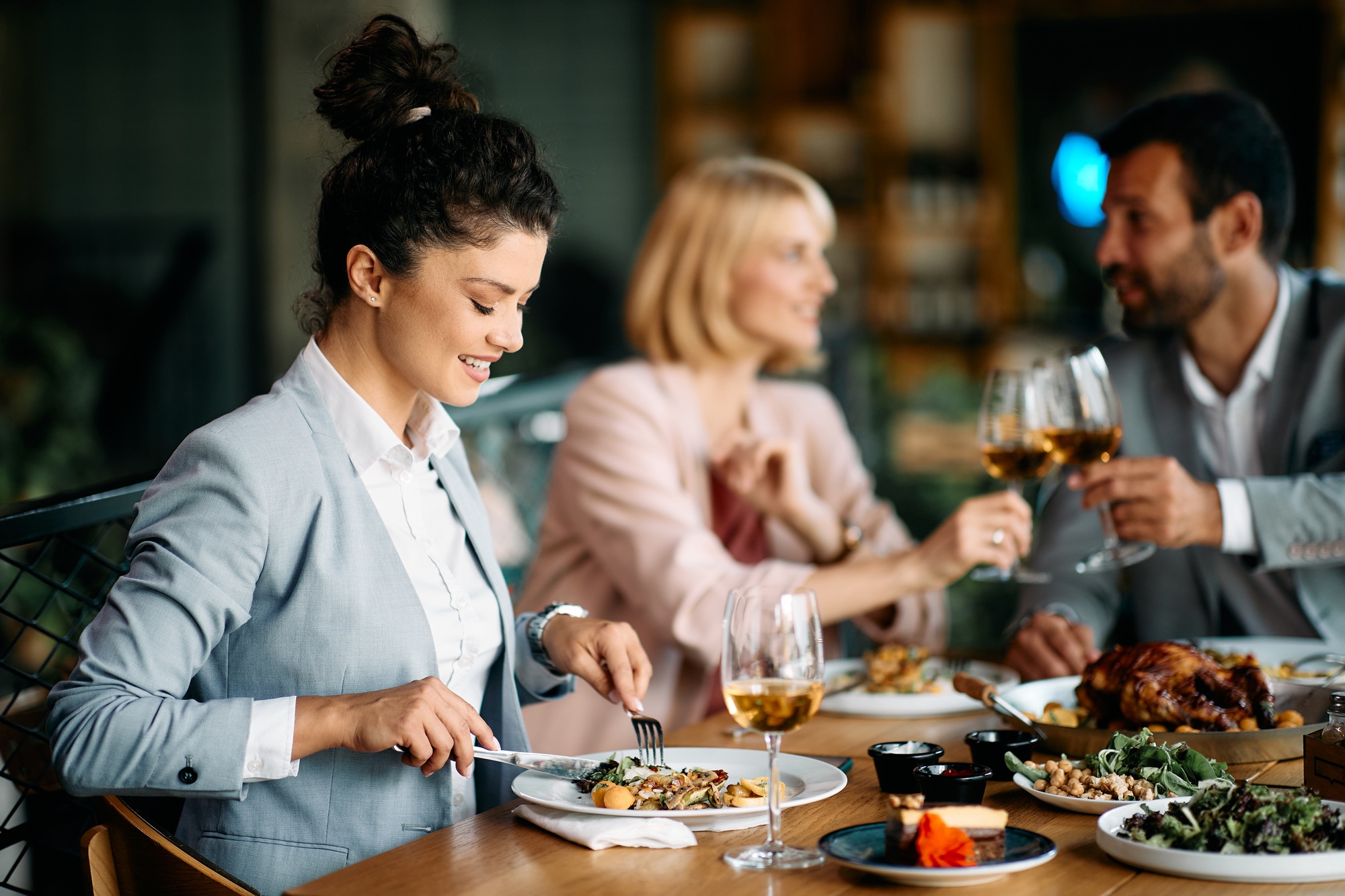 Happy businesswoman eating while having lunch with coworkers in a restaurant.