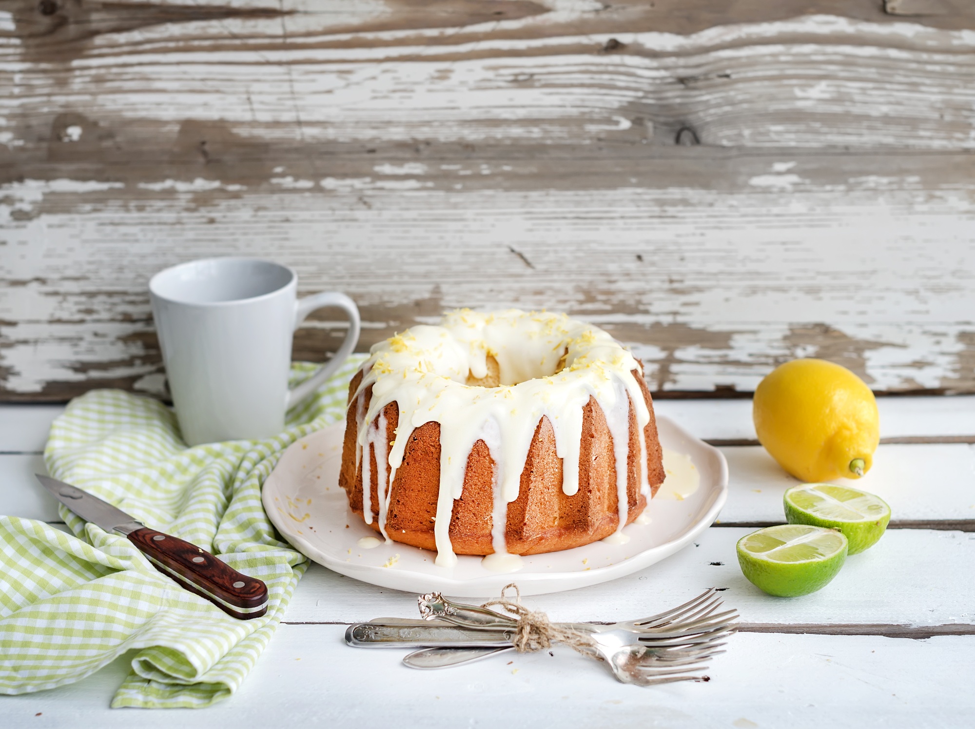 Moist lime and lemon bundt yoghurt cake, white rustic wooden background.