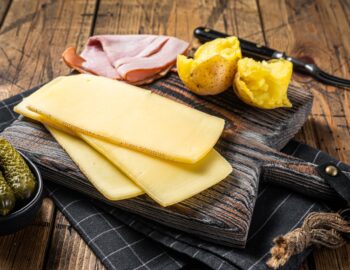 Ready for cooking Raclette Swiss cheese slices with boiled potato and ham.