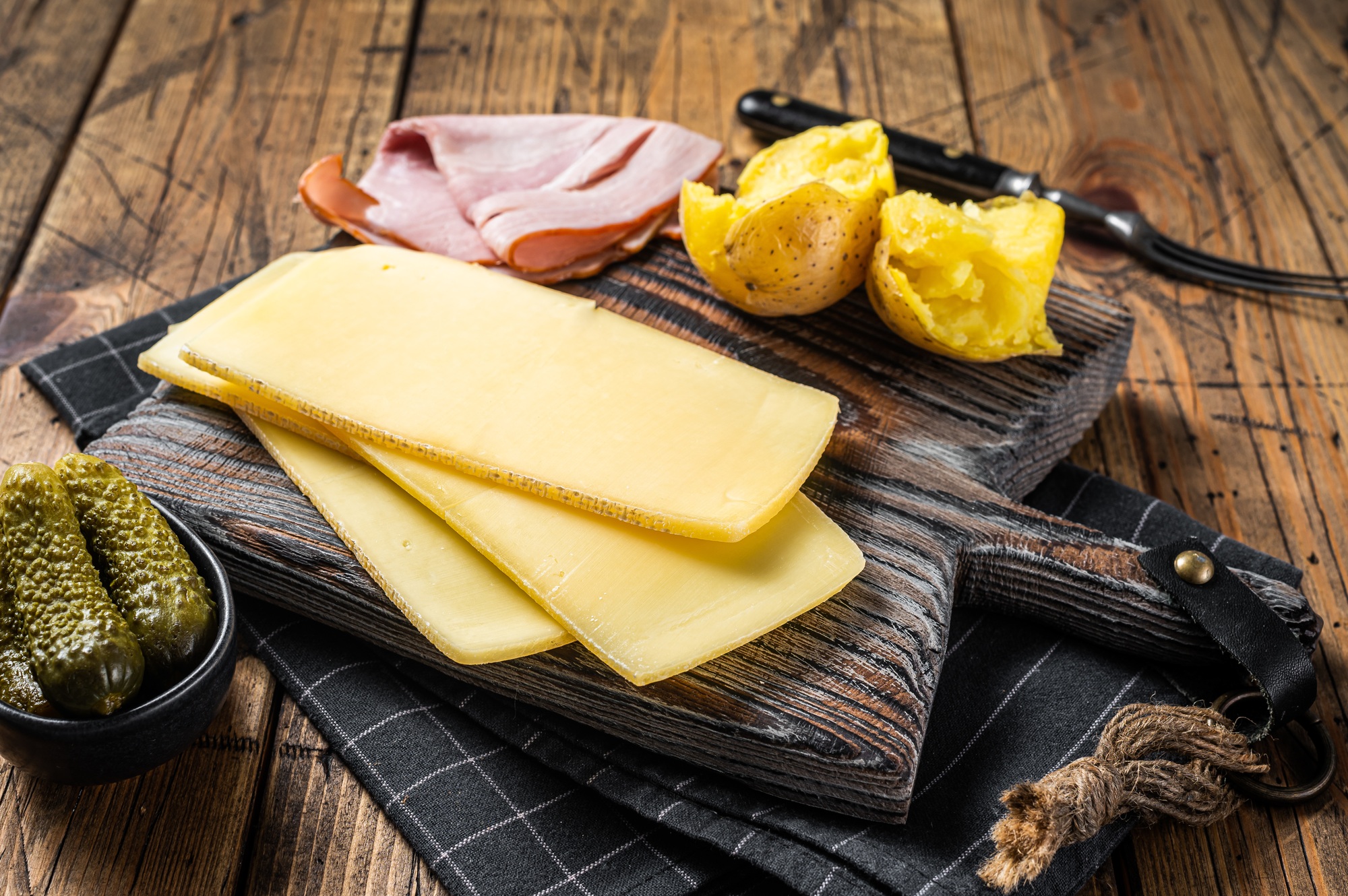 Ready for cooking Raclette Swiss cheese slices with boiled potato and ham.