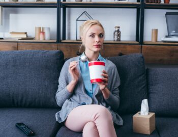 surprised woman eating ice cream and looking at camera while siitng on couch at home alone